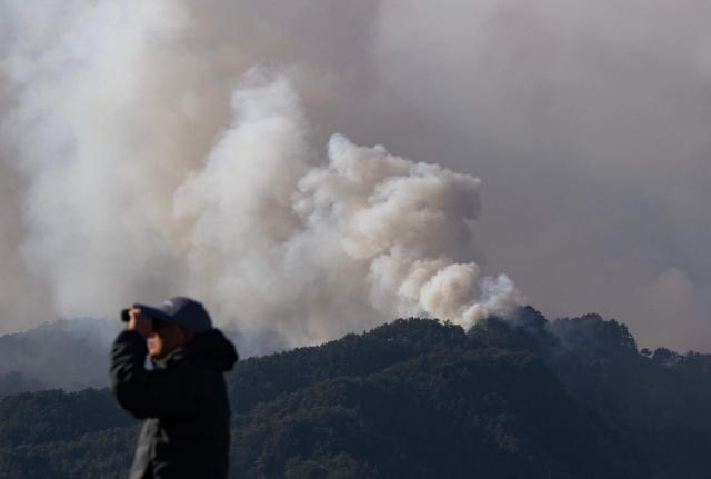 A man uses binoculars to look at different parts of the fire burning around the town of Otsuchi in Iwate Prefecture on April 25, 2026. Hundreds of firefighters were battling wildfires in the forests of northern Japan on April 25, as authorities urged more than 3,200 people to evacuate from their homes, government officials said. (Photo by ANDREW CABALLERO-REYNOLDS / AFP)