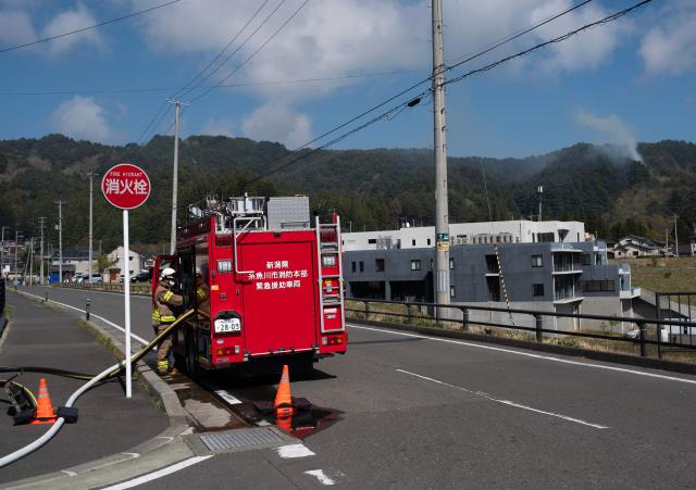 A firefighter refills his fire truck as smoke is seen in the background in the town of Otsuchi in Iwate Prefecture on April 25, 2026. Hundreds of firefighters were battling wildfires in the forests of northern Japan on April 25, as authorities urged more than 3,200 people to evacuate from their homes, government officials said. (Photo by ANDREW CABALLERO-REYNOLDS / AFP)