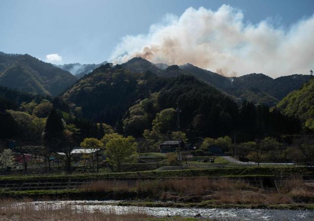 Houses are seen at the base of a mountain as a forest fire burns at the top near the town of Otsuchi in Iwate Prefecture on April 25, 2026. Hundreds of firefighters were battling wildfires in the forests of northern Japan on April 25, as authorities urged more than 3,200 people to evacuate from their homes, government officials said. (Photo by ANDREW CABALLERO-REYNOLDS / AFP)