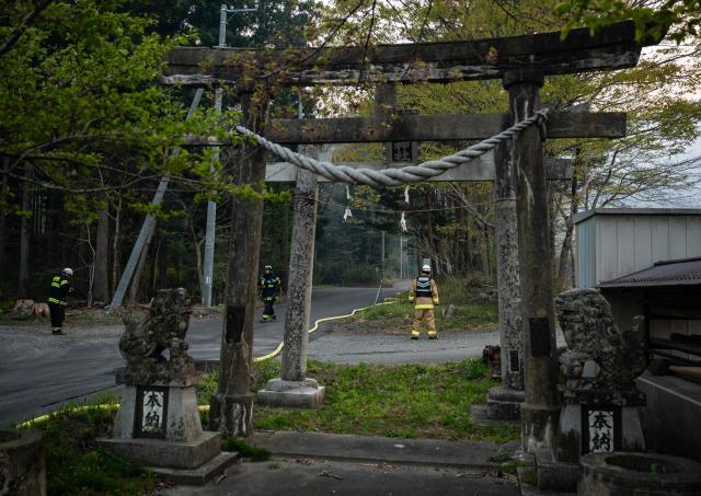 Firefighters lay water hoses down the road to crews in the woods in Kirikiri in Iwate Prefecture on April 25, 2026. Hundreds of firefighters were battling wildfires in the forests of northern Japan on April 25, as authorities urged more than 3,200 people to evacuate from their homes, government officials said. (Photo by ANDREW CABALLERO-REYNOLDS / AFP)