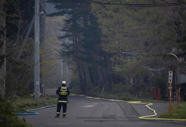 A firefighter checks the pressure on a water hose going to a crew in the woods in Kirikiri in Iwate Prefecture on April 25, 2026. Hundreds of firefighters were battling wildfires in the forests of northern Japan on April 25, as authorities urged more than 3,200 people to evacuate from their homes, government officials said. (Photo by ANDREW CABALLERO-REYNOLDS / AFP)