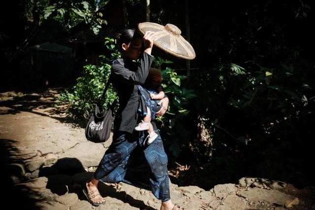A woman of the Baduy ethnic group, known for maintaining ancestral customs and the limited use of modern technology, makes shade for her baby as she walks in Kanekes, Banten province on April 24, 2026. The Baduy people are an indigenous community in western Java, divided into the Inner Baduy, who wear white and follow stricter traditional customs, and the Outer Baduy, who typically wear dark clothing and have more interaction with the outside world. (Photo by YASUYOSHI CHIBA / AFP)
