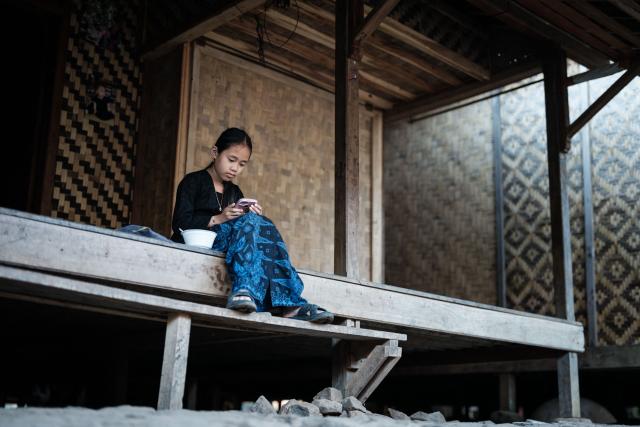 A girl of the Baduy ethnic group, known for maintaining ancestral customs and the limited use of modern technology, uses a smartphone in Kanekes, Banten province on April 24, 2026. The Baduy people are an indigenous community in western Java, divided into the Inner Baduy, who wear white and follow stricter traditional customs, and the Outer Baduy, who typically wear dark clothing and have more interaction with the outside world. (Photo by YASUYOSHI CHIBA / AFP)