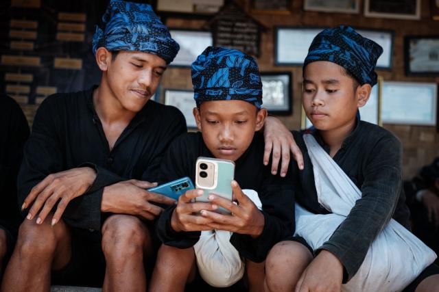 Members of the Baduy ethnic group, known for maintaining ancestral customs and the limited use of modern technology, use a smartphone before departing for a venue about 40 km away for their traditional harvest thanksgiving ceremony in Kanekes, Banten province on April 24, 2026. The Baduy people are an indigenous community in western Java, divided into the Inner Baduy, who wear white and follow stricter traditional customs, and the Outer Baduy, who typically wear dark clothing and have more interaction with the outside world. (Photo by YASUYOSHI CHIBA / AFP)