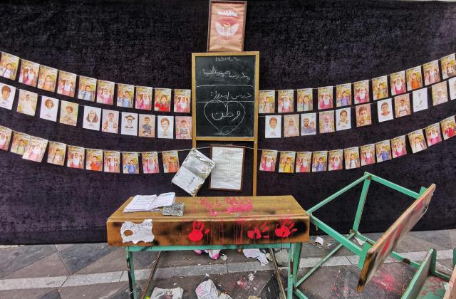 Images of children killed on the first day of the war in an alleged US-Israeli missile strike on a school in the southern Iranian city of Minab, are strung along the wall behind overturned school desks at a mosque in the capital Tehran on April 25, 2026. On February 28, Israel and the United States launched strikes on Iran, killing its supreme leader and triggering a war that spread across the Middle East. (Photo by ATTA KENARE / AFP) / 