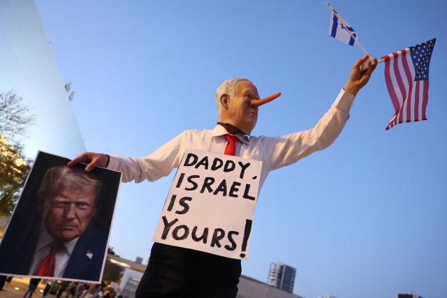 An Israeli left-wing activist, disguised as the Israeli Prime Minister Benjamin Netanyahu and holding an image of the US President Donald Trump and the US flag, demonstrates in HaBima Square against the ongoing war with Iran and against the Israeli government, in Tel Aviv on April 25, 2026. Since the ceasefire between Israel, the United States, and Iran came into effect, a relative calm has prevailed, with no bombings reported in Iran or the Gulf, after five weeks of conflict that left thousands dead, primarily in Iran and Lebanon. (Photo by Jack GUEZ / AFP) / 
