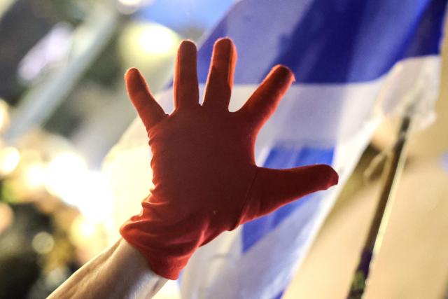 An Israeli left-wing activist holds up a hand in a red glove during a demonstration in HaBima Square against the ongoing war with Iran and against the Israeli government, in Tel Aviv on April 25, 2026. Since the ceasefire between Israel, the United States, and Iran came into effect, a relative calm has prevailed, with no bombings reported in Iran or the Gulf, after five weeks of conflict that left thousands dead, primarily in Iran and Lebanon. (Photo by Jack GUEZ / AFP) / 