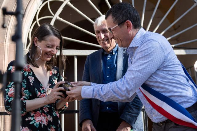 French national Cecile Kohler (L) receives from the hands of Soultz-Haut-Rhin's mayor Marcello Rotolo (R) a honorary medal during a ceremony to symbolically take down a banner displayed on the town hall in her hometown of Soultz-Haut-Rhin, eastern France on April 25, 2026. Cecile Kohler, 41, and Jacques Paris, 72, arrested on espionage charges and imprisoned for almost four years in Iran, returned home on April 8, 2026. (Photo by ROMEO BOETZLE / AFP)