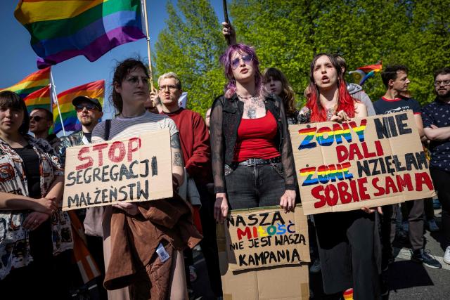 Participants wave rainbow flags and hold a placard reading 'Stop the segregation of married couples', 'Our love is not your campaign' and 'They didn’t give me a wife - I took one myself' during a demonstration of LGBT organisations in Warsaw on April 25, 2026. The LGBT organisations point out that the Polish government has not implemented landmark rulings of the European Court of Human Rights that require Poland to recognize same-sex marriages concluded in other EU member states. (Photo by Wojtek RADWANSKI / AFP)