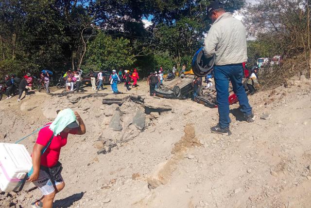 People walk past vehicles destroyed by a bomb attack at El Tunel, on the Popayan-Cali road, in Cajibio, Cauca department, Colombia, on April 25, 2026. A bomb attack on April 25 left seven people dead and 20 injured in an area of Colombia with a strong guerrilla presence, amid a spate of attacks just over a month before the presidential elections, the governor of the Cauca region said. (Photo by Francisco Calderon / AFP)