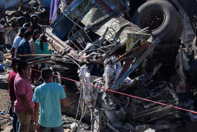 People stand next to vehicles destroyed by a bomb attack at El Tunel, on the Popayan-Cali road, in Cajibio, Cauca department, Colombia, on April 25, 2026. A bomb attack on April 25 left seven people dead and 20 injured in an area of Colombia with a strong guerrilla presence, amid a spate of attacks just over a month before the presidential elections, the governor of the Cauca region said. (Photo by Francisco Calderon / AFP)