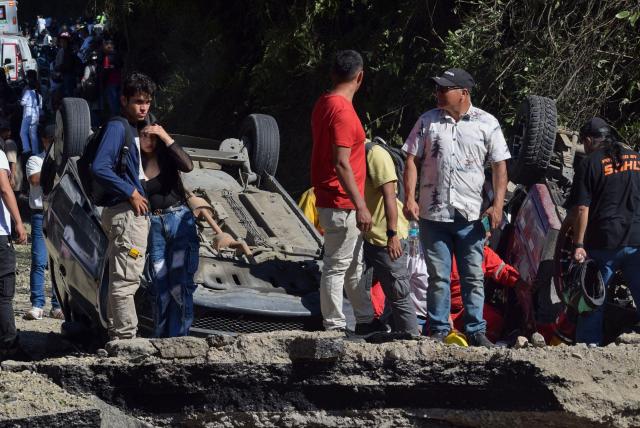 People stand next to vehicles destroyed by a bomb attack at El Tunel, on the Popayan-Cali road, in Cajibio, Cauca department, Colombia, on April 25, 2026. A bomb attack on April 25 left seven people dead and 20 injured in an area of Colombia with a strong guerrilla presence, amid a spate of attacks just over a month before the presidential elections, the governor of the Cauca region said. (Photo by Francisco Calderon / AFP)