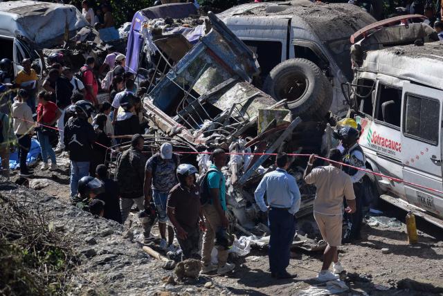 People stand next to vehicles destroyed by a bomb attack at El Tunel, on the Popayan-Cali road, in Cajibio, Cauca department, Colombia, on April 25, 2026. A bomb attack on April 25 left seven people dead and 20 injured in an area of Colombia with a strong guerrilla presence, amid a spate of attacks just over a month before the presidential elections, the governor of the Cauca region said. (Photo by Francisco Calderon / AFP)