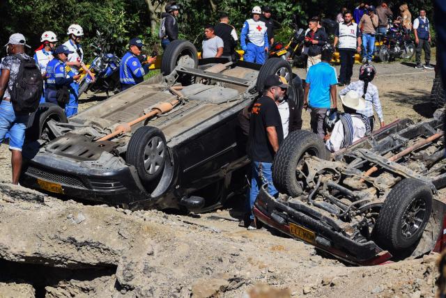 People stand next to vehicles destroyed by a bomb attack at El Tunel, on the Popayan-Cali road, in Cajibio, Cauca department, Colombia, on April 25, 2026. A bomb attack on April 25 left seven people dead and 20 injured in an area of Colombia with a strong guerrilla presence, amid a spate of attacks just over a month before the presidential elections, the governor of the Cauca region said. (Photo by Francisco Calderon / AFP)