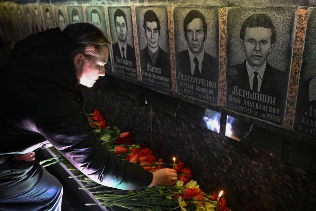 A woman places a candle in front of a memorial for Chernobyl victims, during a commemoration ceremony marking the 40th anniversary of the explosion at the Chernobyl nuclear power plant, the worst civilian nuclear disaster in history, in the town of Slavutych on April 26, 2026, amid the Russian invasion of Ukraine. (Photo by Genya SAVILOV / AFP)
