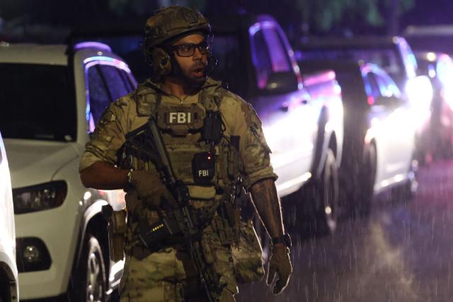 An FBI tactical agent keeps watch as they prepare to leave the investigation scene near a house associated with the suspected White House Correspondents Dinner shooter in Torrance, California, early on April 26, 2026. US Secret Service agents bundled Donald Trump from the stage as shots rang out Saturday evening at a media gala, in what the president later described as an attack by a "would-be assassin." Armed guards opened fire at the gunman who charged through a security checkpoint just outside the ballroom of the hotel where Trump, First Lady Melania Trump, senior government officials and hundreds of other black-tie guests had gathered. (Photo by Patrick T. Fallon / AFP)