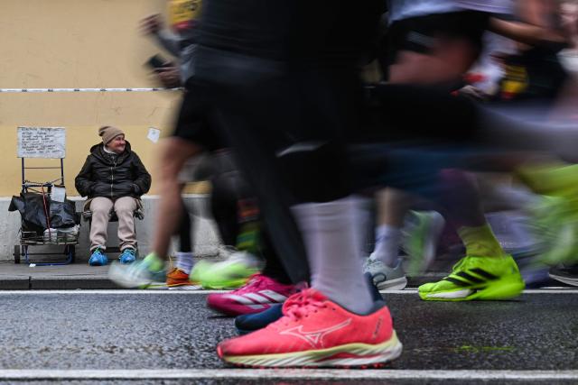 Participants of the Moscow Half Marathon run along Bolshaya Ordynka street past a woman begging for alms in central Moscow on April 26, 2026. (Photo by Igor IVANKO / AFP)