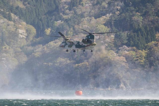 A Japan Self Defense Force helicopter loads up on water near the town of Otsuchi in Iwate Prefecture on April 26, 2026. Hundreds of firefighters were battling wildfires in the forests of northern Japan, as authorities urged more than 3,200 people to evacuate from their homes, government officials said. (Photo by ANDREW CABALLERO-REYNOLDS / AFP)