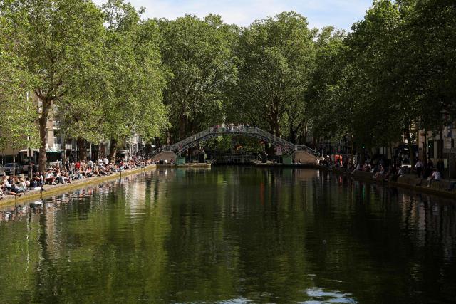 People sit by the Canal Saint-Martin in Paris on April 26, 2026. (Photo by Charlotte SIEMON / AFP)