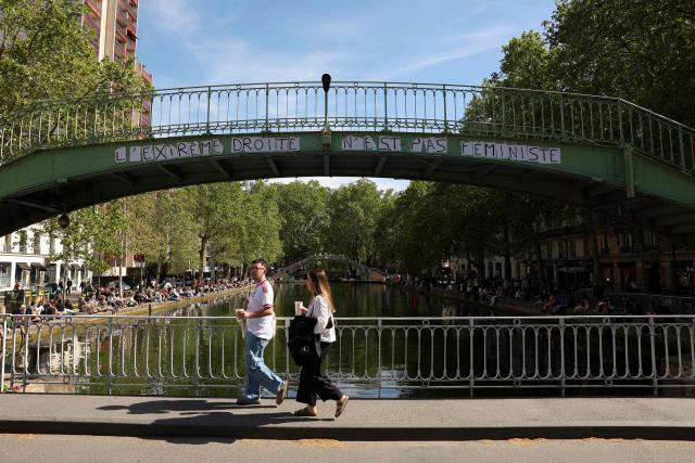 Pedestrians walk on a bridge past a collage reading "The far right is not feminist" as they cross the Canal Saint-Martin in Paris on April 26, 2026. (Photo by Charlotte SIEMON / AFP)