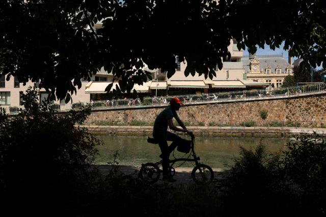 A cyclist rides his bike past the Canal de l'Ourcq in Pantin, suburb of Paris on April 26, 2026. (Photo by Charlotte SIEMON / AFP)