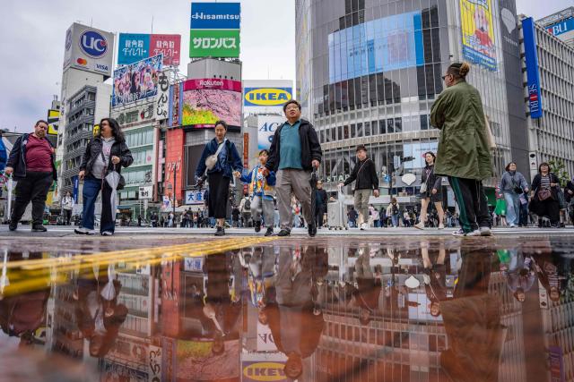People cross the Shibuya Crossing as their reflection shimmers in a puddle in Tokyo on April 27, 2026. (Photo by Yuichi YAMAZAKI / AFP)