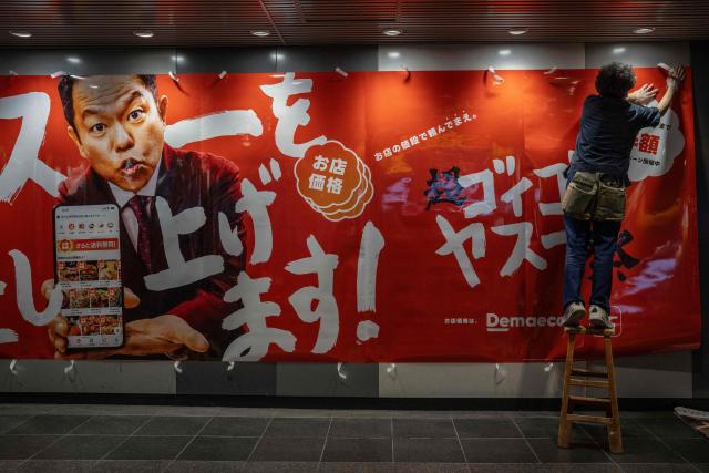 A worker installs a food delivery service advertisement on a wall at a station in Tokyo on April 27, 2026. (Photo by Yuichi YAMAZAKI / AFP)