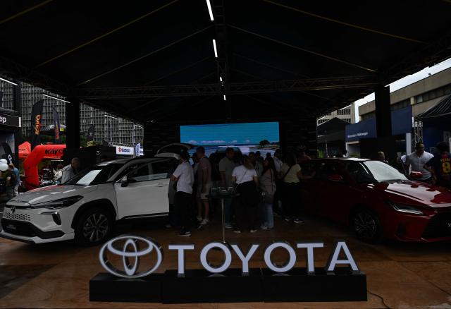 A logo of the Japanese Toyota Motor Corporation is seen while visitors look at new cars priced in U.S. dollars during the 14th edition of Venezuela’s largest automotive exhibition, "AutoFest 2026," at the Centro Comercial Ciudad Tamanaco (CCCT) in Caracas on April 26, 2026. (Photo by Juan BARRETO / AFP)