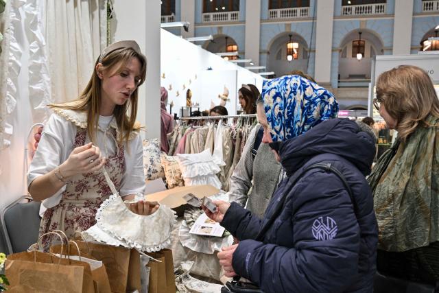 A seller (L) shows clothes to a visitor at the fair of folk and arts crafts of Russia, in central Moscow on March 4, 2026. (Photo by Hector RETAMAL / AFP)