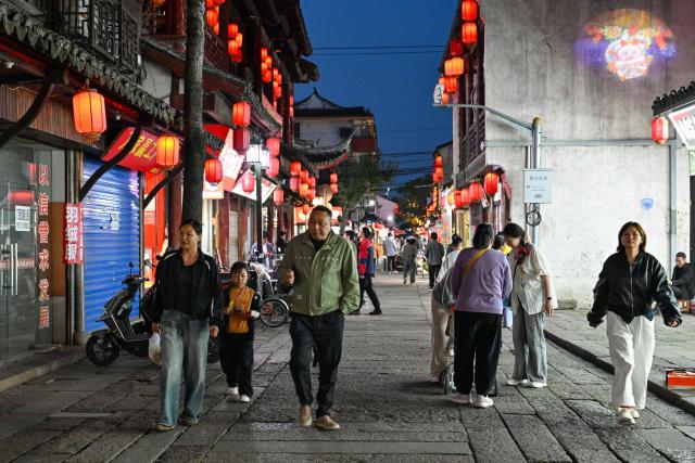 People walk along a street as they visit the Fengjing Ancient Town on the outskirts of Shanghai on April 26, 2026. (Photo by ADEK BERRY / AFP)