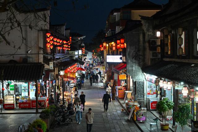People walk along a street as they visit the Fengjing Ancient Town on the outskirts of Shanghai on April 26, 2026. (Photo by ADEK BERRY / AFP)