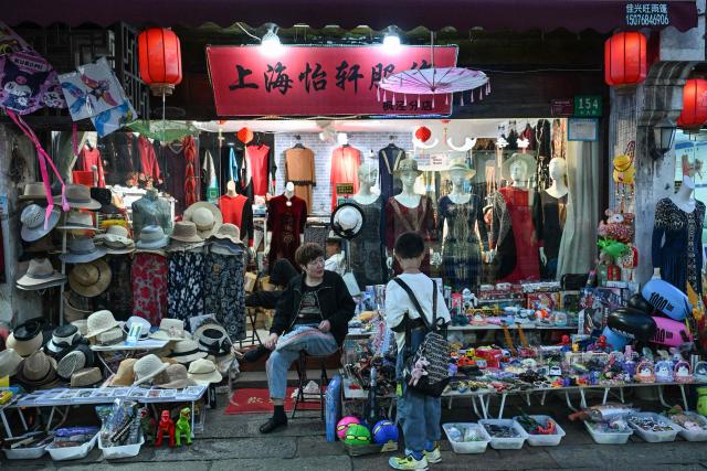 Vendors wait for customers as people visit the Fengjing Ancient Town on the outskirts of Shanghai on April 26, 2026. (Photo by ADEK BERRY / AFP)