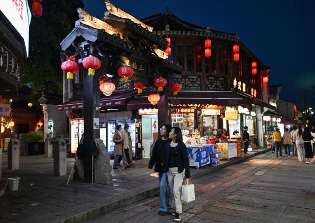 People walk along a street as they visit the Fengjing Ancient Town on the outskirts of Shanghai on April 26, 2026. (Photo by ADEK BERRY / AFP)