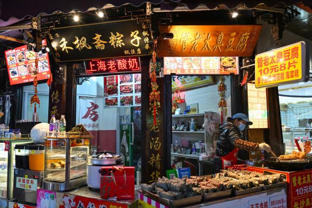 A food vendor fries snacks as people visit the Fengjing Ancient Town on the outskirts of Shanghai on April 26, 2026. (Photo by ADEK BERRY / AFP)