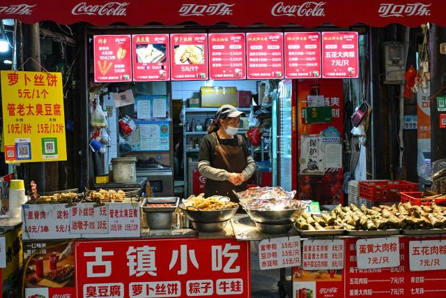 A food vendor waits for customers as people visit the Fengjing Ancient Town on the outskirts of Shanghai on April 26, 2026. (Photo by ADEK BERRY / AFP)