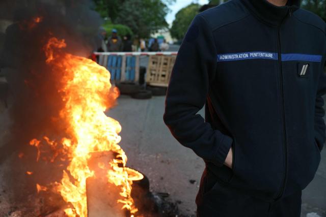 A striking prison guard stands by a fire while others block access to the Bois-d'Arcy detention center, west of Paris, on April 27, 2026, after the Ufap-Unsa union called for a blockade of prisons to draw attention to prison overcrowding and “fill the 5,000 vacant positions.” (Photo by Alain JOCARD / AFP)