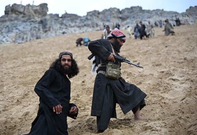 Taliban security personnel climb barefoot up a steep and sandy mountainside on a weekend at the Sayad area of Reg-e-Rawan in Kapisa province on April 24, 2026. Hundreds of visitors travel each weekend to Reg-e-Rawan -- "the moving sands" in Dari -- to practice parkour or roll down the honey-coloured sand in Kapisa province and to unwind beside breathtaking views. (Photo by Wakil KOHSAR / AFP)