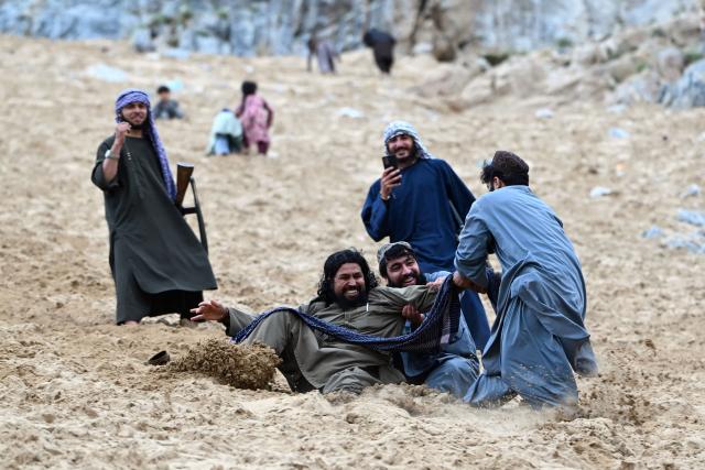 Taliban security personnel enjoy rolling down a steep and sandy mountainside on a weekend at the Sayad area of Reg-e-Rawan in Kapisa province on April 24, 2026. Hundreds of visitors travel each weekend to Reg-e-Rawan -- "the moving sands" in Dari -- to practice parkour or roll down the honey-coloured sand in Kapisa province and to unwind beside breathtaking views. (Photo by Wakil KOHSAR / AFP)