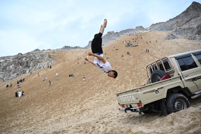 An Afghan parkour athlete performs a stunt on the back of a vehicle on a weekend in the sandy mountainside at the Sayad area of Reg-e-Rawan in Kapisa province on April 24, 2026. Hundreds of visitors travel each weekend to Reg-e-Rawan -- "the moving sands" in Dari -- to practice parkour or roll down the honey-coloured sand in Kapisa province and to unwind beside breathtaking views. (Photo by Wakil KOHSAR / AFP)