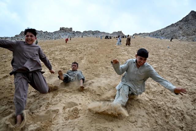 TOPSHOT - Afghan visitors enjoy rolling down a steep and sandy mountainside on a weekend at the Sayad area of Reg-e-Rawan in Kapisa province on April 24, 2026. Hundreds of visitors travel each weekend to Reg-e-Rawan -- "the moving sands" in Dari -- to practice parkour or roll down the honey-coloured sand in Kapisa province and to unwind beside breathtaking views. (Photo by Wakil KOHSAR / AFP)