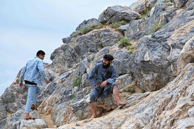 Taliban security personnel rest as they climb barefoot up a steep mountainside on a weekend at the Sayad area of Reg-e-Rawan in Kapisa province on April 24, 2026. Hundreds of visitors travel each weekend to Reg-e-Rawan -- "the moving sands" in Dari -- to practice parkour or roll down the honey-coloured sand in Kapisa province and to unwind beside breathtaking views. (Photo by Wakil KOHSAR / AFP)