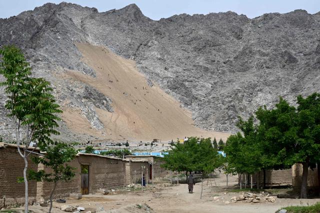 An Afghan man walks past houses near a steep and sandy mountainside at the Sayad area of Reg-e-Rawan in Kapisa province on April 24, 2026. Hundreds of visitors travel each weekend to Reg-e-Rawan -- "the moving sands" in Dari -- to practice parkour or roll down the honey-coloured sand in Kapisa province and to unwind beside breathtaking views. (Photo by Wakil KOHSAR / AFP)