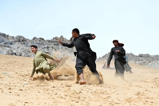 This photograph taken on April 17, 2026 shows Afghan visitors running down a steep and sandy mountainside at the Sayad area of Reg-e-Rawan in Kapisa province. Hundreds of visitors travel each weekend to Reg-e-Rawan -- "the moving sands" in Dari -- to practice parkour or roll down the honey-coloured sand in Kapisa province and to unwind beside breathtaking views. (Photo by Wakil KOHSAR / AFP)