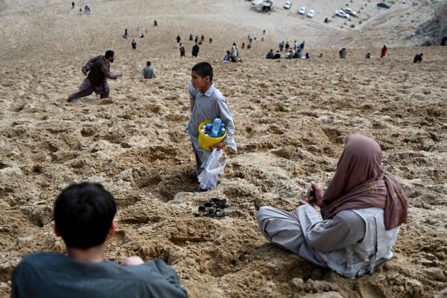 An Afghan boy selling refreshments looks for customers as visitors enjoy the view of a steep and sandy mountainside on a weekend at the Sayad area of Reg-e-Rawan in Kapisa province on April 24, 2026. Hundreds of visitors travel each weekend to Reg-e-Rawan -- "the moving sands" in Dari -- to practice parkour or roll down the honey-coloured sand in Kapisa province and to unwind beside breathtaking views. (Photo by Wakil KOHSAR / AFP)