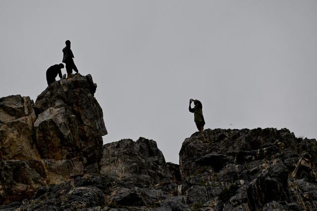 An Afghan visitors take photos on a mountainside at the Sayad area of Reg-e-Rawan in Kapisa province on April 24, 2026. Hundreds of visitors travel each weekend to Reg-e-Rawan -- "the moving sands" in Dari -- to practice parkour or roll down the honey-coloured sand in Kapisa province and to unwind beside breathtaking views. (Photo by Wakil KOHSAR / AFP)