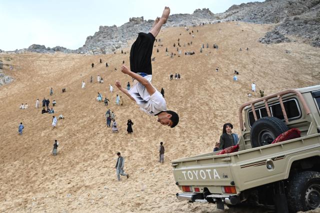 An Afghan parkour athlete performs a stunt on the back of a vehicle on a weekend in the sandy mountainside at the Sayad area of Reg-e-Rawan in Kapisa province on April 24, 2026. Hundreds of visitors travel each weekend to Reg-e-Rawan -- "the moving sands" in Dari -- to practice parkour or roll down the honey-coloured sand in Kapisa province and to unwind beside breathtaking views. (Photo by Wakil KOHSAR / AFP)