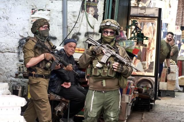 A palestinian man looks on as Israeli soldiers patrol the market in the Old City of Nablus, in the northern Israeli-occupied West Bank on April 27, 2026. In 2025, the Israeli military installed around 1,000 gates at the entrances of Palestinian towns and villages which, when closed, cut off residents from access to services they rely on in nearby larger local municipalities. Palestinians have pointed  to worsening access to water, roads and basic services as Jewish settlements -- considered illegal under international law -- spread across the West Bank. (Photo by Jaafar ASHTIYEH / AFP)