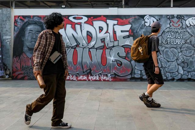 Visitors walk past a mural featuring Andrie Yunus, the deputy coordinator of the KontraS rights group who suffered serious injuries when two men on a scooter threw acid at him, at a Mural Exhibition, "From Citizens for Andrie", in Jakarta, on April 27, 2026. The head of Indonesia's military intelligence has stepped down after four members of his unit were arrested over an acid attack on an activist critical of the military's growing role in government, according to a spokesman from the armed forces. (Photo by BAY ISMOYO / AFP)