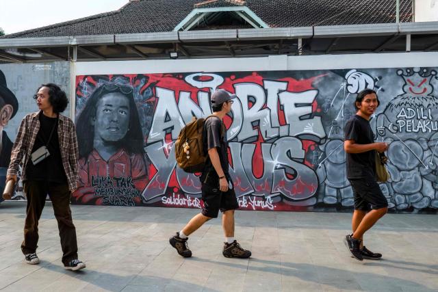 Visitors walk past a mural featuring Andrie Yunus, the deputy coordinator of the KontraS rights group who suffered serious injuries when two men on a scooter threw acid at him, at a Mural Exhibition, "From Citizens for Andrie", in Jakarta, on April 27, 2026. The head of Indonesia's military intelligence has stepped down after four members of his unit were arrested over an acid attack on an activist critical of the military's growing role in government, according to a spokesman from the armed forces. (Photo by BAY ISMOYO / AFP)