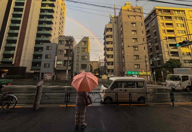 A woman stops on a sidewalk to look at a rainbow seen between apartment buildings in Tokyo on April 27, 2026. (Photo by Andrew CABALLERO-REYNOLDS / AFP)